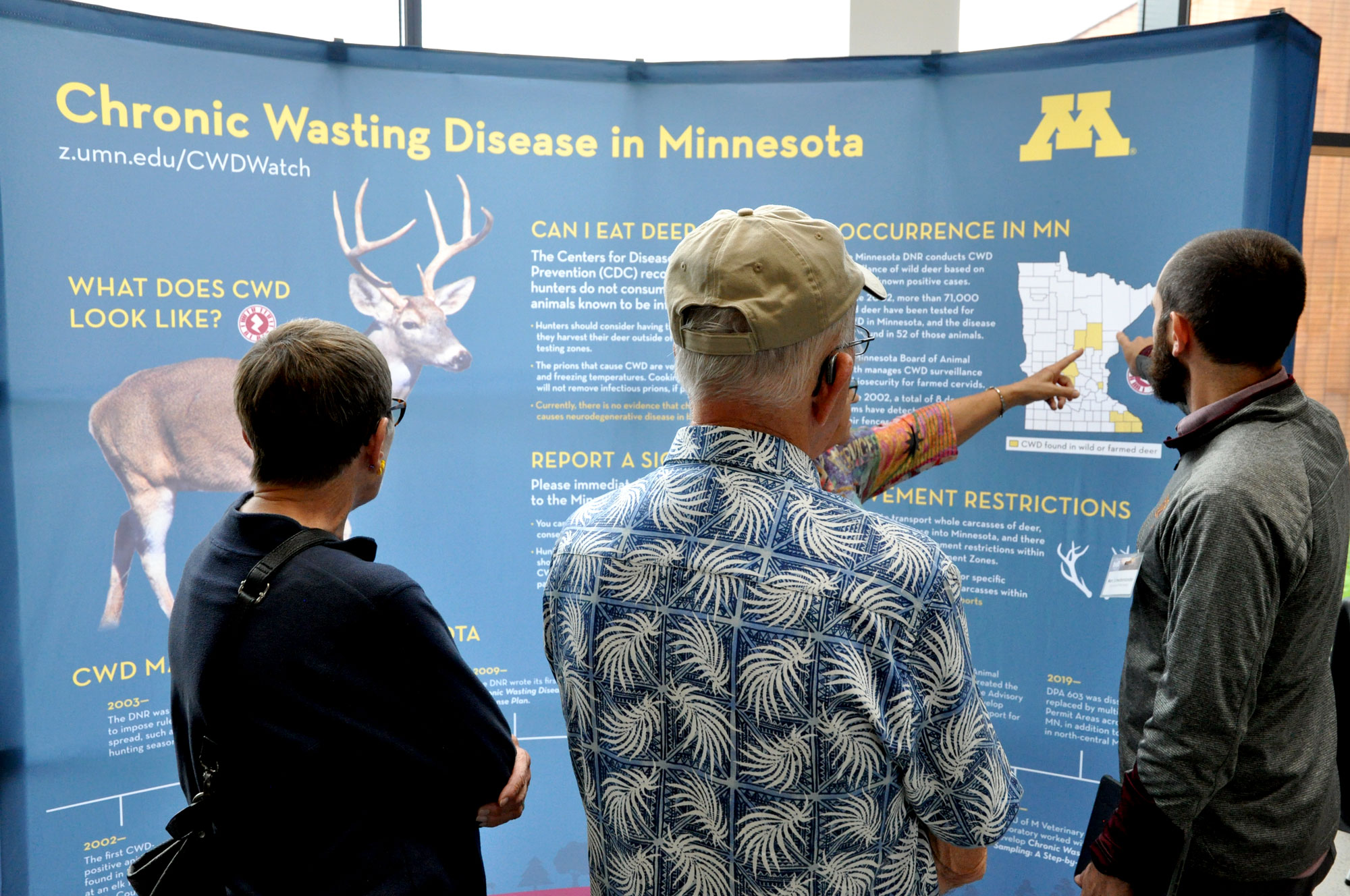 3 people looking at an information display to learn about CWD at the Bell Museum event